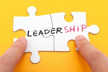 Hand holding two matching white paper jigsaw puzzles which written leadership word